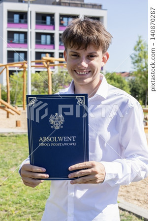 Smiling teenage student graduate celebrating primary education completion, holding folder text in Polish language saying elementary school graduate. Smiling teenage student graduate celebrating primary education completion, holding folder text in Polish language saying elementary school graduate. 140870287