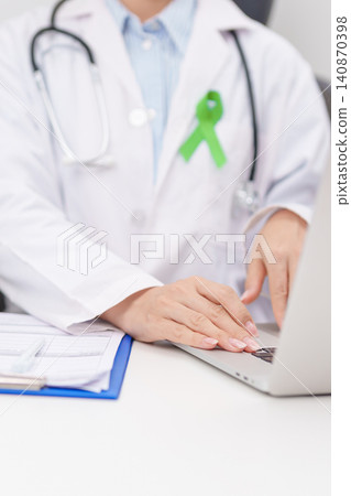 doctor using laptop and report notes on notebook. lime Green Ribbon for concept of May Celiac Awareness month, Lyme disease, September Lymphoma, Mental Health Awareness month and October Liver cancer 140870398