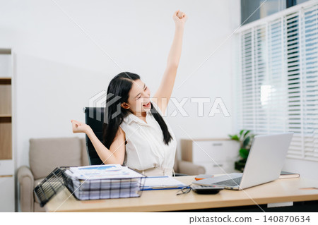 Smiling young businesswoman celebrating success at her desk with laptop, showcasing achievement, productivity, happiness, remote work and professional growth. Smiling young businesswoman celebrating success at her desk with laptop, showcasing achievement, productivity, happiness, remote work and professional growth. 140870634