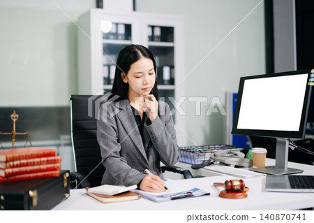 Asian female lawyer reading a legal book and working with a computer at an office desk Asian female lawyer reading a legal book and working with a computer at an office desk 140870741