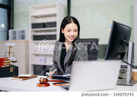 Asian female lawyer reading a legal book and working with a computer at an office desk Asian female lawyer reading a legal book and working with a computer at an office desk 140870745