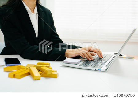 Professional working on laptop with gold bars on desk. Investment, finance, trading, wealth growth, market strategy and modern business concept. Professional working on laptop with gold bars on desk. Investment, finance, trading, wealth growth, market strategy and modern business concept. 140870790