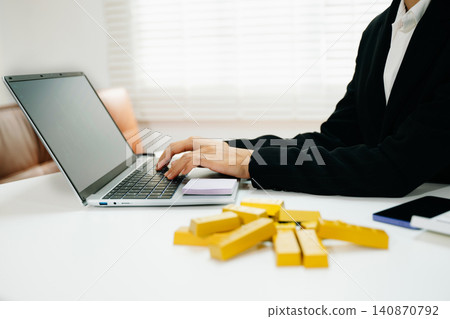 Professional working on laptop with gold bars on desk. Investment, finance, trading, wealth growth, market strategy and modern business concept. Professional working on laptop with gold bars on desk. Investment, finance, trading, wealth growth, market strategy and modern business concept. 140870792