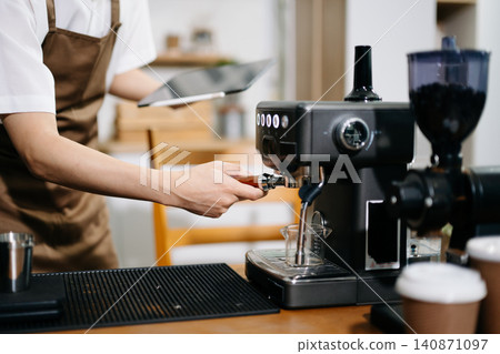 Professional cafe owner preparing coffee in a modern coffee shop with espresso machine and digital tablet, showcasing small business lifestyle Professional cafe owner preparing coffee in a modern coffee shop with espresso machine and digital tablet, showcasing small business lifestyle 140871097