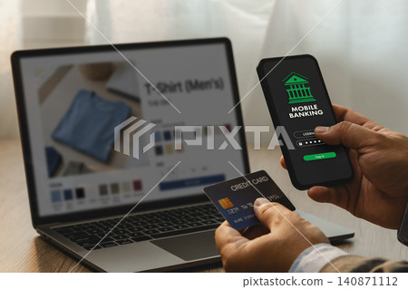 Hand using smartphone mobile banking login beside credit card and laptop shopping page for online payment, account transaction, digital finance, financial service, and business banking. Hand using smartphone mobile banking login beside credit card and laptop shopping page for online payment, account transaction, digital finance, financial service, and business banking. 140871112