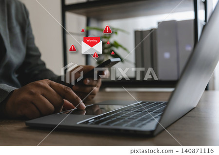 Hand holds smartphone beside laptop with warning email alert icons, phishing message notice, spam notification and cybersecurity risk concept for online security review in office workspace. Hand holds smartphone beside laptop with warning email alert icons, phishing message notice, spam notification and cybersecurity risk concept for online security review in office workspace. 140871116