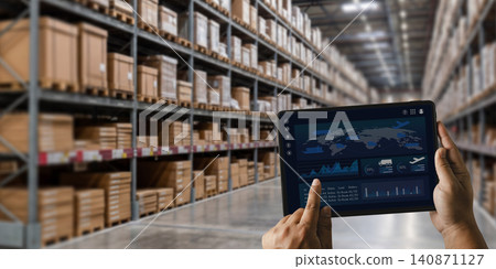 Hands hold a tablet dashboard in a warehouse aisle to track inventory, monitor logistics, analyze supply chain data, and support storage management with connected distribution operations. Hands hold a tablet dashboard in a warehouse aisle to track inventory, monitor logistics, analyze supply chain data, and support storage management with connected distribution operations. 140871127