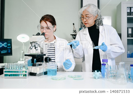 Two diverse female scientists analyze biological samples in a modern lab, utilizing a microscope and petri dishes Two diverse female scientists analyze biological samples in a modern lab, utilizing a microscope and petri dishes 140871533