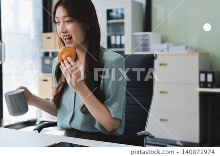 Asian woman reading book eating snack in office Asian woman reading book eating snack in office 140871974