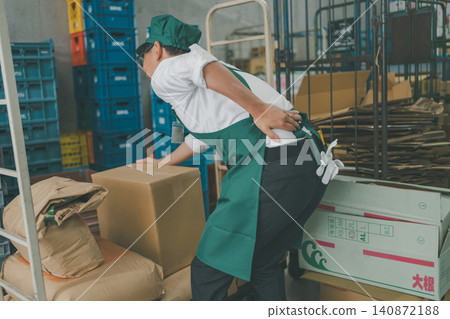A male staff member in the back room of a supermarket is seen holding his back with his hand after hurting it. 140872188