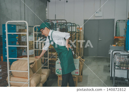 A male staff member injures his back in the back room of a supermarket. A male staff member injures his back in the back room of a supermarket. 140872812