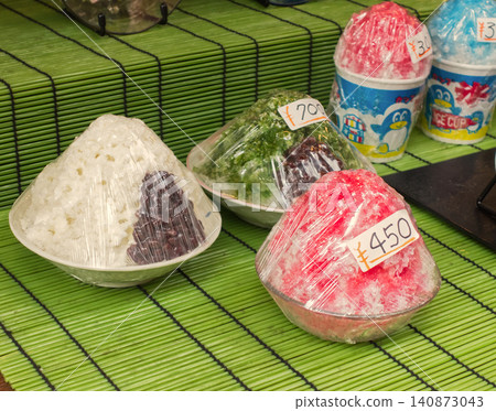 A food sample of shaved ice wrapped in plastic wrap, displayed in front of a retro Showa-era restaurant. 140873043