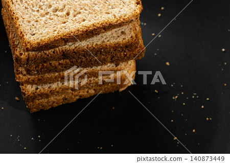 Stack of toasted whole wheat bread slices on a black plate with crumbs. 140873449