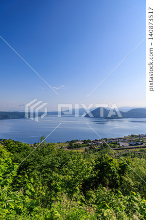 A breathtaking view of the town of Toyako Onsen and Nakajima Island against the backdrop of a clear blue sky and the beautiful Lake Toya. A breathtaking view of the town of Toyako Onsen and Nakajima Island against the backdrop of a clear blue sky and the beautiful Lake Toya. 140873517