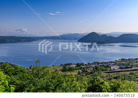 北海道的一處風景優美的地方,湖畔溫泉小鎮被鬱鬱蔥蔥的夏季綠植環繞,毗鄰廣闊的火山口湖。 北海道的一處風景優美的地方,湖畔溫泉小鎮被鬱鬱蔥蔥的夏季綠植環繞,毗鄰廣闊的火山口湖。 140873518