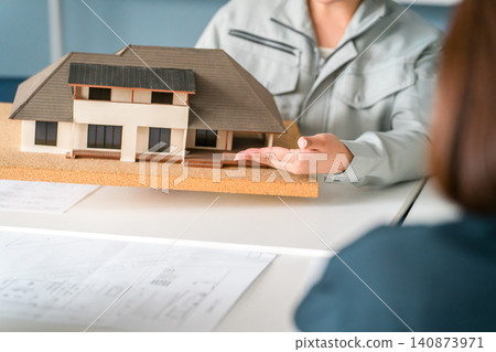 來自建築業的男女商務人士身著工作服,使用住宅模型進行商務談判、解釋和演示。 來自建築業的男女商務人士身著工作服,使用住宅模型進行商務談判、解釋和演示。 140873971