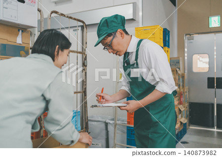 一名男性收貨員正在填寫收據,一名女性收貨員正在超市後倉清點商品。 一名男性收貨員正在填寫收據,一名女性收貨員正在超市後倉清點商品。 140873982