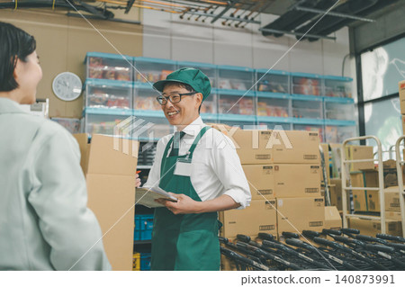 A male staff member was smiling and talking while checking the invoices in the back room. A male staff member was smiling and talking while checking the invoices in the back room. 140873991
