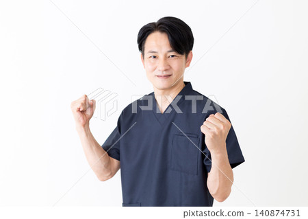 一位身穿海軍藍手術服的中年男性針灸師/整骨師做出了一個勝利的手勢。 一位身穿海軍藍手術服的中年男性針灸師/整骨師做出了一個勝利的手勢。 140874731