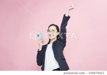 一位女商人看著她的智慧型手機，做出了一個得意的手勢。 140874821