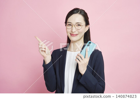 一位微笑的女商人拿著智慧型手機，指向左邊。 140874823
