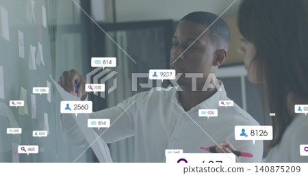 Holding paper and placing sticky note, man in white shirt working at glass wall with analytics Holding paper and placing sticky note, man in white shirt working at glass wall with analytics 140875209