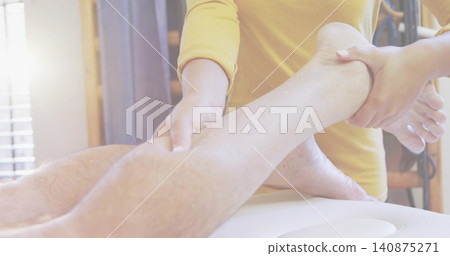 Stretching therapist holding patient lower leg and foot on padded table, hands, mustard top, blinds Stretching therapist holding patient lower leg and foot on padded table, hands, mustard top, blinds 140875271