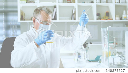 Pipetting senior researcher holding beaker with yellow liquid at research lab bench, wearing PPE Pipetting senior researcher holding beaker with yellow liquid at research lab bench, wearing PPE 140875327