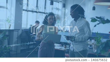 Coworkers reviewing laptop in modern office by windows, holding tablet and wearing sleeveless top Coworkers reviewing laptop in modern office by windows, holding tablet and wearing sleeveless top 140875632