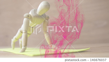Balancing wooden mannequin doing diagonal crawl pose on yellow pad on table, with pink powder plume Balancing wooden mannequin doing diagonal crawl pose on yellow pad on table, with pink powder plume 140876037