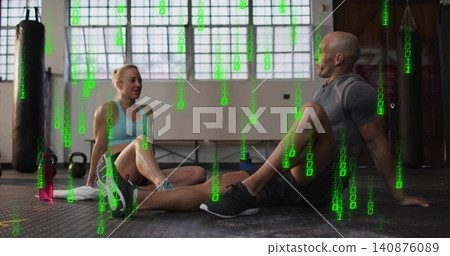 Sitting pair wearing athletic clothes on rubber gym floor, with heavy bags and green binary overlay Sitting pair wearing athletic clothes on rubber gym floor, with heavy bags and green binary overlay 140876089
