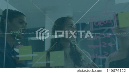 Writing middle woman holding marker, team in sweaters writing on glass board in office with postits Writing middle woman holding marker, team in sweaters writing on glass board in office with postits 140876122