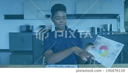 Holding pie chart, woman in navy blouse pointing to paper on kitchenette table with bar chart Holding pie chart, woman in navy blouse pointing to paper on kitchenette table with bar chart 140876130