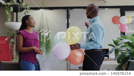 Arranging pastel balloons, coworkers wearing blue dress shirt and purple blouse decorating office Arranging pastel balloons, coworkers wearing blue dress shirt and purple blouse decorating office 140876154