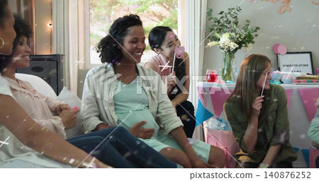 Smiling women sitting around pregnant woman wearing light dress at home holding prop sticks Smiling women sitting around pregnant woman wearing light dress at home holding prop sticks 140876252