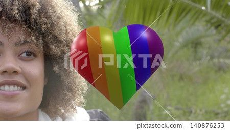 Smiling woman wearing light hoodie gazing at glossy rainbow heart in garden, copy space Smiling woman wearing light hoodie gazing at glossy rainbow heart in garden, copy space 140876253