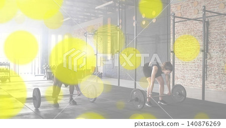 Preparing two partners lifting barbells in CrossFit gym, female tank, male tee, yellow bokeh Preparing two partners lifting barbells in CrossFit gym, female tank, male tee, yellow bokeh 140876269
