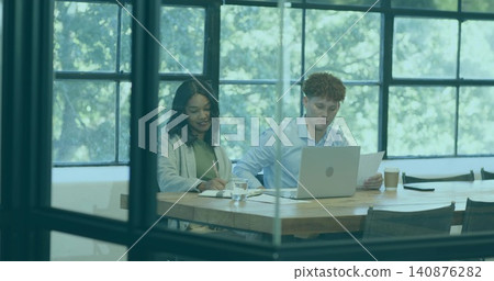 Writing woman in light blazer, man in blue shirt reviewing prints at glass office, laptop notebook Writing woman in light blazer, man in blue shirt reviewing prints at glass office, laptop notebook 140876282