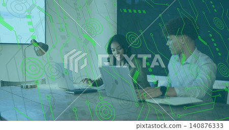 Discussing woman wearing blazer and man wearing shirt using laptops at office table, green overlay Discussing woman wearing blazer and man wearing shirt using laptops at office table, green overlay 140876333