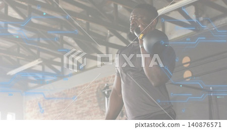 Lifting dark-shirted man racking kettlebell on right-shoulder in gym with AR overlay, copy space Lifting dark-shirted man racking kettlebell on right-shoulder in gym with AR overlay, copy space 140876571