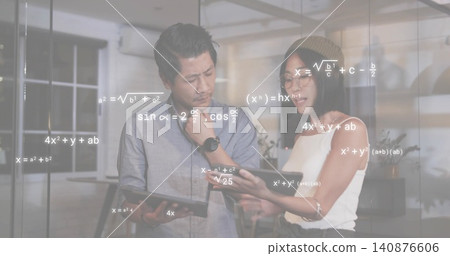 Examining tablets, two colleagues in shirt and beanie working in glass office, formulas appearing Examining tablets, two colleagues in shirt and beanie working in glass office, formulas appearing 140876606