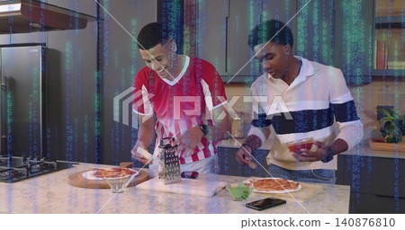 Two men in striped, banded tops grating, topping pizzas with box grater in kitchen, code overlay 140876810