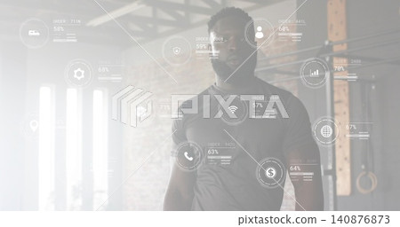 Standing fit man wearing dark fitted athletic shirt in warehouse gym, HUD, pull-up rig, rings Standing fit man wearing dark fitted athletic shirt in warehouse gym, HUD, pull-up rig, rings 140876873