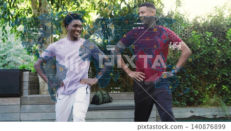 Standing two men in sportswear facing each other, smiling on patio, duffel and holographic map 140876899