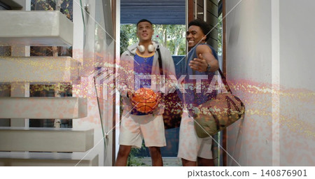 Standing two men holding basketball, carrying duffel in entryway, wearing hoodie and sleeveless top Standing two men holding basketball, carrying duffel in entryway, wearing hoodie and sleeveless top 140876901