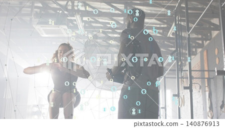 Jumping woman doing squat at industrial gym, coach in hoodie holding phone, rig and digital overlay Jumping woman doing squat at industrial gym, coach in hoodie holding phone, rig and digital overlay 140876913