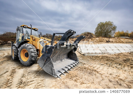 Universal excavator loader performs tasks at a construction site by moving soil and clearing land for upcoming development projects in outdoor space Universal excavator loader performs tasks at a construction site by moving soil and clearing land for upcoming development projects in outdoor space 140877089
