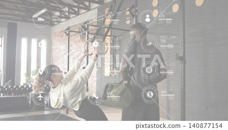 Leaning trainee in sportswear using rings doing row in studio, trainer with green duffel bag, HUD Leaning trainee in sportswear using rings doing row in studio, trainer with green duffel bag, HUD 140877154
