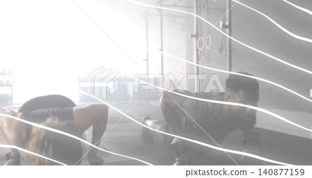 Two adults performing partnered push-ups on handles at gym, wearing sports top, leggings, shorts Two adults performing partnered push-ups on handles at gym, wearing sports top, leggings, shorts 140877159