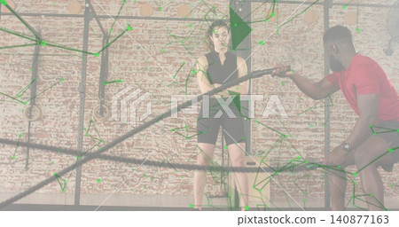 Standing woman wearing black sleeveless top and shorts listening at gym, with battle rope overlay Standing woman wearing black sleeveless top and shorts listening at gym, with battle rope overlay 140877163